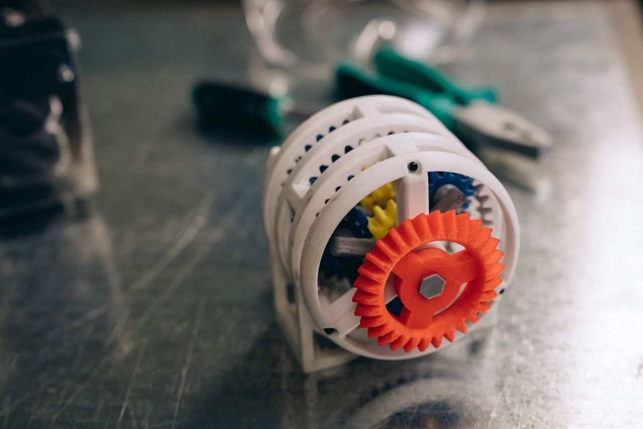 About A close-up photo of a 3D printed gear mechanism on a metallic workbench, highlighting innovation and technology.