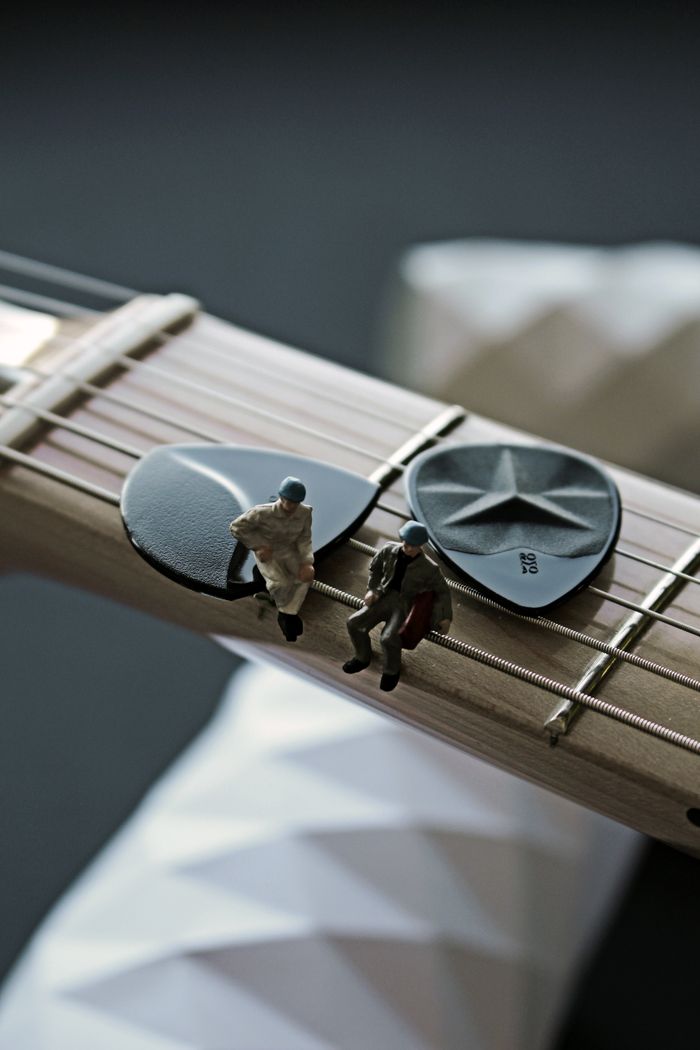 Services Miniature toys positioned on guitar neck with guitar picks.
